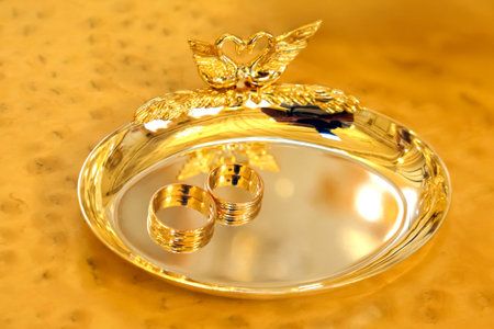 Two shining wedding rings rest on a polished gold tray featuring a decorative swan design, set in an intimate indoor space that reflects warmth and love, perfect for a special occasion.の写真素材