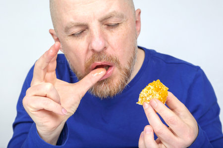 A man in a blue shirt is savoring a piece of honeycomb, closing his eyes as he tastes its sweetness.