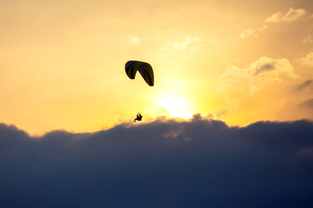 A person glides gracefully with a colorful parachute against a backdrop of clouds and a vibrant...