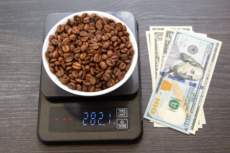 A white bowl filled with roasted coffee beans sits on a digital scale displaying 282.1 grams, with US dollar bills placed beside it on a dark wooden surfaceの写真素材