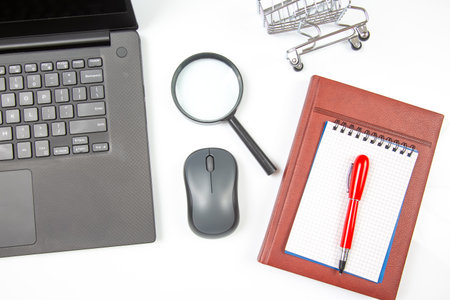 Laptop, magnifying glass, computer mouse, smartphone, pen, notepad on a white background. Items for business and online shoppingの写真素材