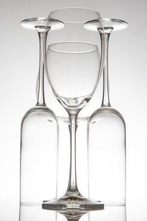 Crystal-clear wine glasses with delicate stems line up, their reflections enhancing the composition on a glossy surface against a neutral gray backdrop.の写真素材
