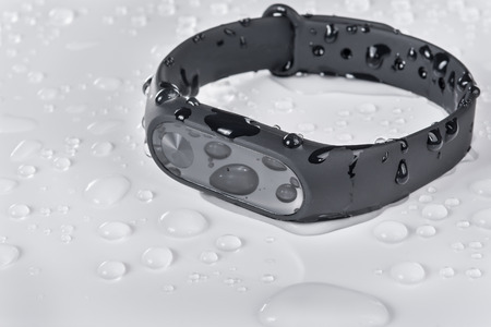 Wet fitness bracelet, fitness tracker on a white glossy background with drops of water
