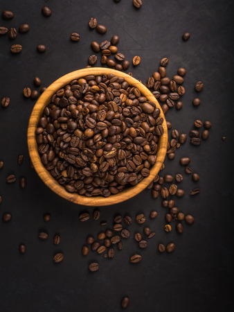 Fresh roasted coffee beans in a wooden bowl on a black stone background top view with copy space.の写真素材