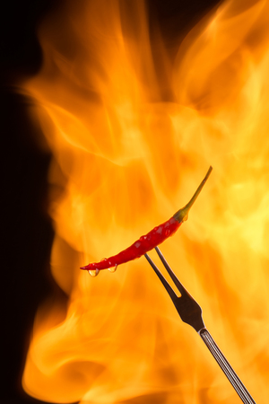 Chilli pepper on meat fork with flame behind on black backgroundの写真素材