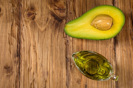 Avocado oil in a glass bowl and fresh avocado on old wooden background. Healthy eating, diet, body care concept. Space for text. Top view.の写真素材