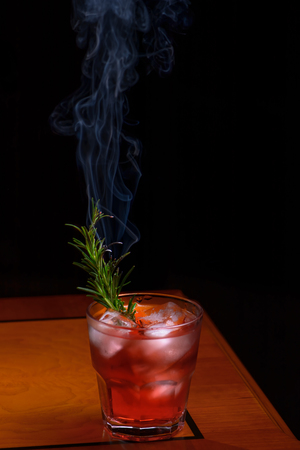 Rosemary smoked negroni cocktail. Negroni cocktail glass on wooden table with branch smoking rosemaryの写真素材