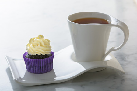 Cupcake in purple wrap and cup of tea on white natural marble table top with copy space.