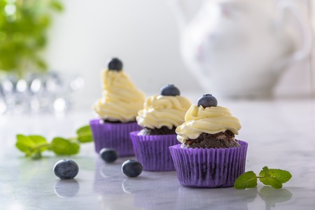 Three cupcakes with blueberry in purple wrap on white marble table.の写真素材