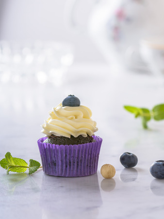 Cupcake with blueberry and hazelnut in purple paper on white natural marble surface.の写真素材