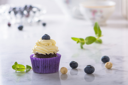 Cupcake with blueberry, hazelnut and mint leaves in purple wrap on marble table top.の写真素材