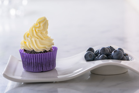 Cupcake on white plate with blueberry in purple wrap on white marble table top.の写真素材