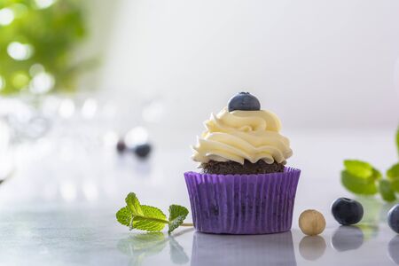 Cupcake with blueberry, hazelnut and mint leaves in purple wrap on marble table top.の写真素材
