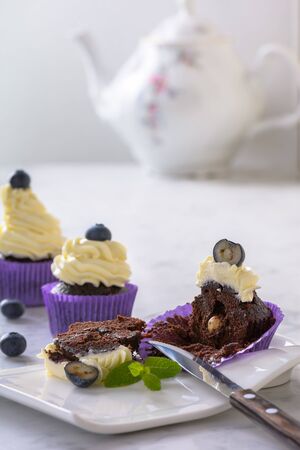Cut cupcake on white plate with blueberry and hazelnut in purple wrap on white marble table top.の写真素材