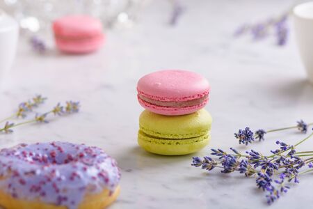Two macarons and sprigs lavender in center of image, one lilac donut in front, one macaron behind, on white marble tableの写真素材