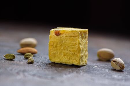 Cube of dessert soan papdi, cardamom grains, pistachios and almond on concrete kitchen worktop.