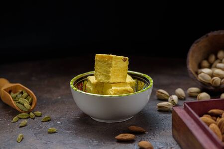 Cubed pyramid of dessert soan papdi, cardamom grains in wooden scoop, pistachios and almond on concrete kitchen surface with space for text.の写真素材