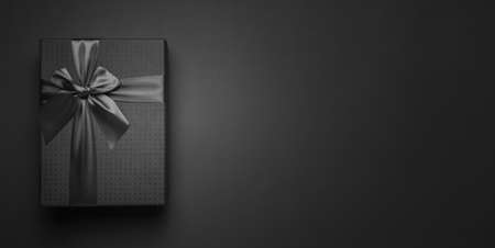 Web banner, advertising header, greeting card with a black gift box tied with a black ribbon on a black background minimalism with place for text, copy space.の写真素材