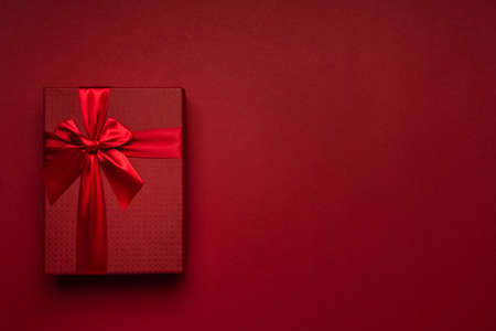 Red gift box with a ribbon on a clean burgundy background with a place for your text, advertising, congratulations.の写真素材