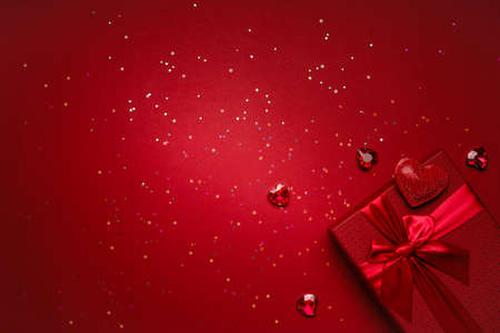 Red gift box tied with a red ribbon for Valentine's Day on a red background with glitter, heart-shaped rhinestones. Beautiful festive background with place for your text.の写真素材