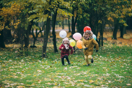 brother and sister running through an autumn park with balloonsの写真素材