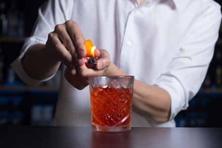 The bartender in a white shirt  makes flame over a cocktail with orange peel. Close-upの写真素材