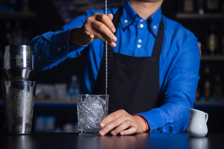 A bartender stirring ingredients in a glass in order to prepare and serve a chilled cocktail at a bar.の写真素材