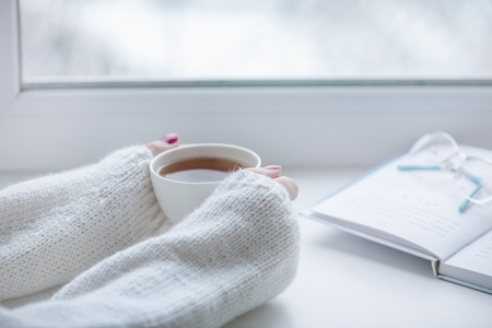 Tea drinking. The woman in a knitted, white pullover holds a cup of hot tea in her hands. Cozy weekends, winter drinks.の写真素材