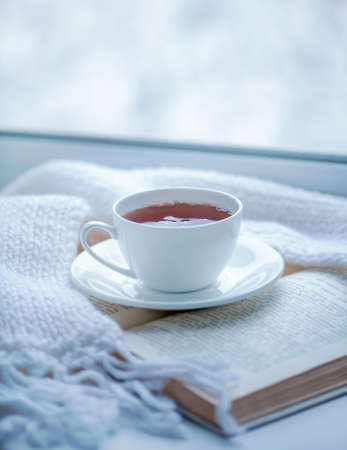 Warm knitted scarf, a cup of hot tea and a bookの写真素材