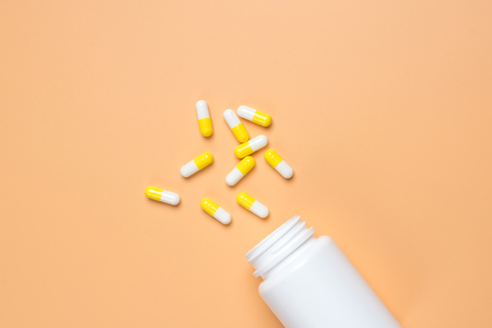Yellow pills, tablets and white bottle on orange background. Copy space for textの写真素材