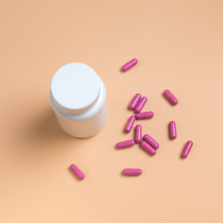 Pink pills, tablets and white bottle on orange background. Copy space for text
