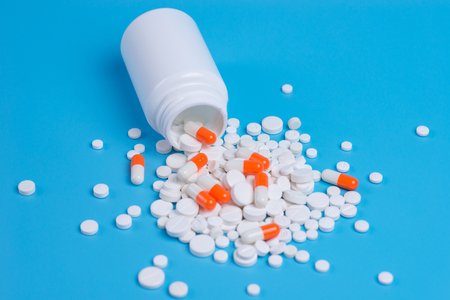White and orange pills, tablets and white bottle on blue background.  Copy space for textの写真素材