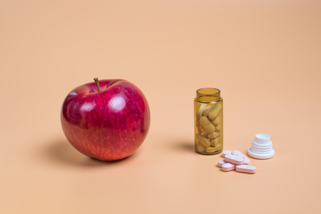 Pink pills in the glass bottle and apple on a orange background. Copy space for textの写真素材