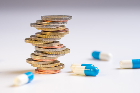 Coins are placed among themselves in different positions next to the blue and white pills. Copy space for textの写真素材