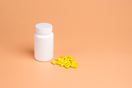 Yellow pills, tablets and white bottle on orange background.  Copy space for textの写真素材