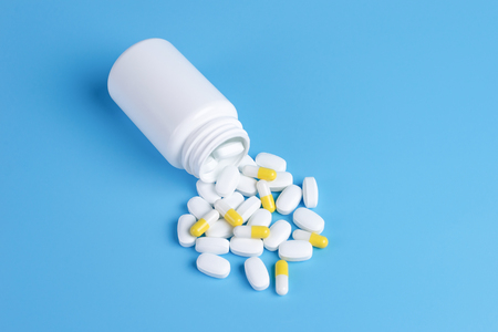 Medicine white and yellow pills or tablets drop out of the white bottle on blue backgroundの写真素材