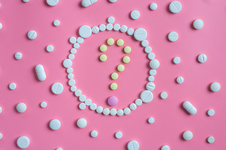 The question mark consists of tablets and white pills on pink background. Copy space for textの写真素材