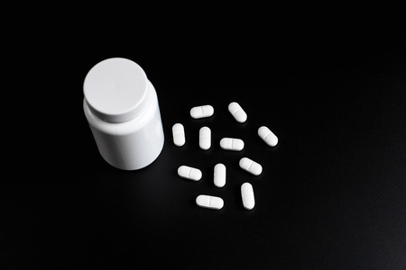 White pills, tablets and white bottle on black background. Copy space for textの写真素材