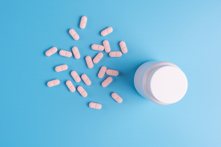 Pink pills, tablets and white bottle on blue background. Copy space for textの写真素材