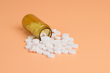 White pills in the brown glass bottle on a orange background. Copy space for text
