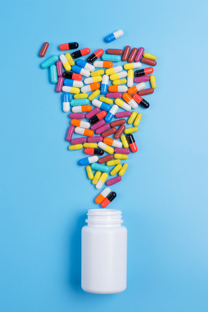 Medicine green, yellow and pink pills or capsules and white bottle on a blue background with copy space.の写真素材