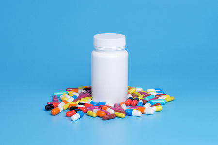 Medicine green, yellow and pink pills or capsules and white bottle on a blue background with copy space.の写真素材