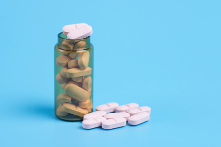 Pink pills in the glass bottle on a blue background. Copy space for textの写真素材