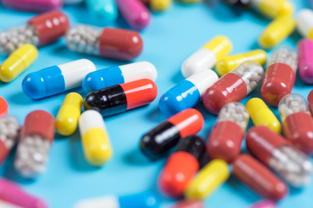 Medicine green, yellow, red and pink pills or capsules on a blue background with copy space.の写真素材
