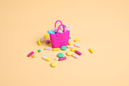 Colored pills fall out of a pink handbag on an orange background. Copy space for textの写真素材