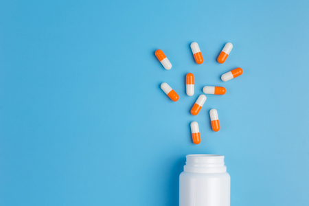 White and orange pills, tablets and white bottle on blue background.  Copy space for text