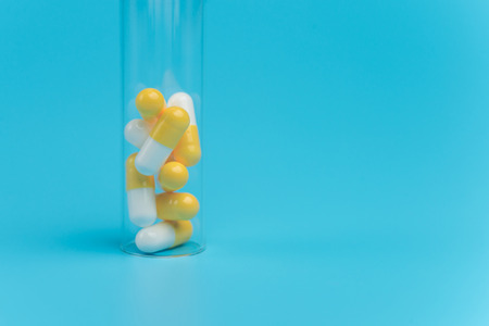 Medicine white and yellow pills in the test tube on blue background. Copy space for textの写真素材