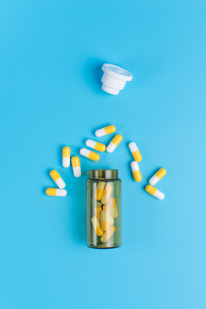 Medicine white and yellow pills or tablets drop out of the brown glass bottle on blue backgroundの写真素材
