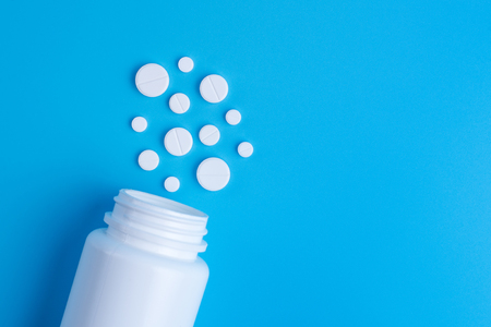 Medicine white pills or tablets drop out of the white bottle on blue backgroundの写真素材