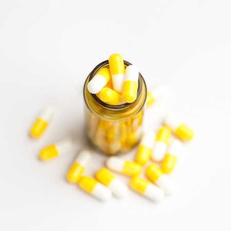 Medicine white and yellow pills or tablets drop out of the brown glass bottle on white background.の写真素材